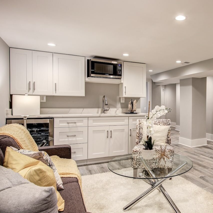 Open living area with white cabinets, microwave, sink, and a round glass coffee table beside a leopard-print chair.