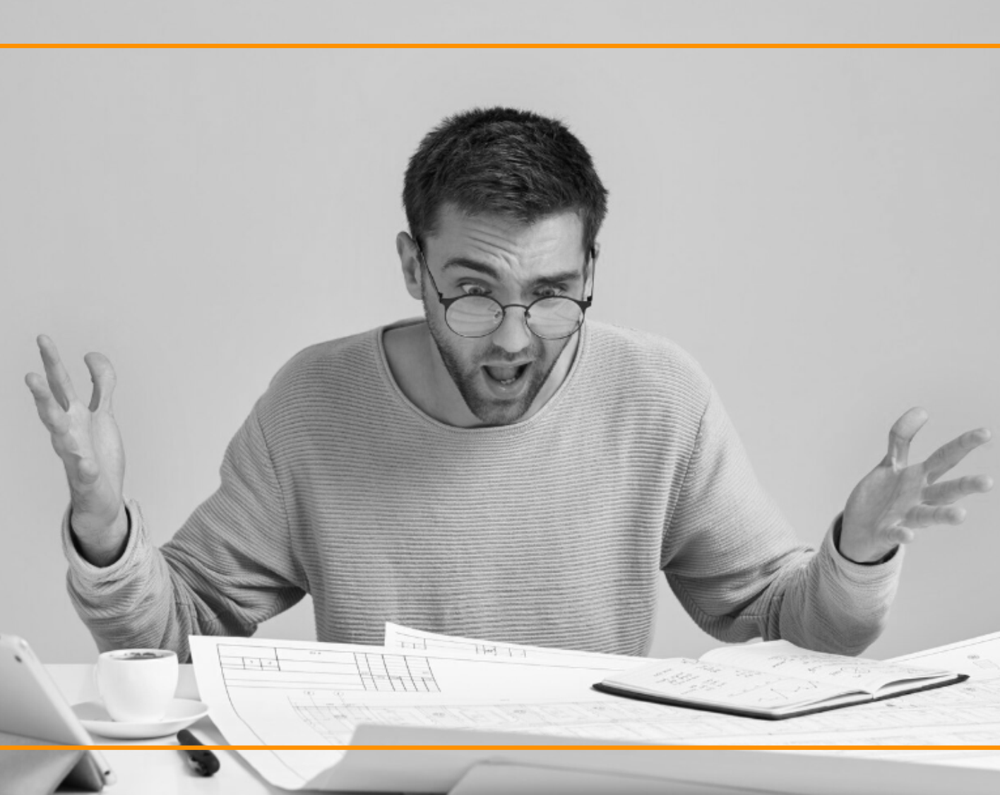 Man with glasses sits at a desk, surrounded by papers, raising hands in surprise at the documents.