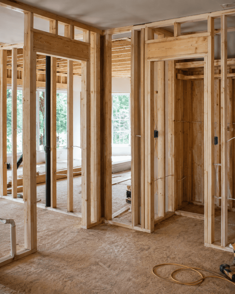 blog » elitebuilding.ca Interior of a house under construction with exposed wooden studs and door frames, wiring, and a visible black pipe along a wall.
